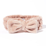The Giovanni Cosmetics PLUSH MULTI-PURPOSE SPA HEADBAND (blush) is a soft, light pink headband with a large bow and non-slip elastic—ideal for keeping hair in place during your beauty routine, shown on a white background.