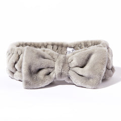 The Giovanni Cosmetics PLUSH MULTI-PURPOSE SPA HEADBAND (gray) features soft, plush fabric with a large front bow and a non-slip elastic band—perfect for your beauty routine, shown against a white background.