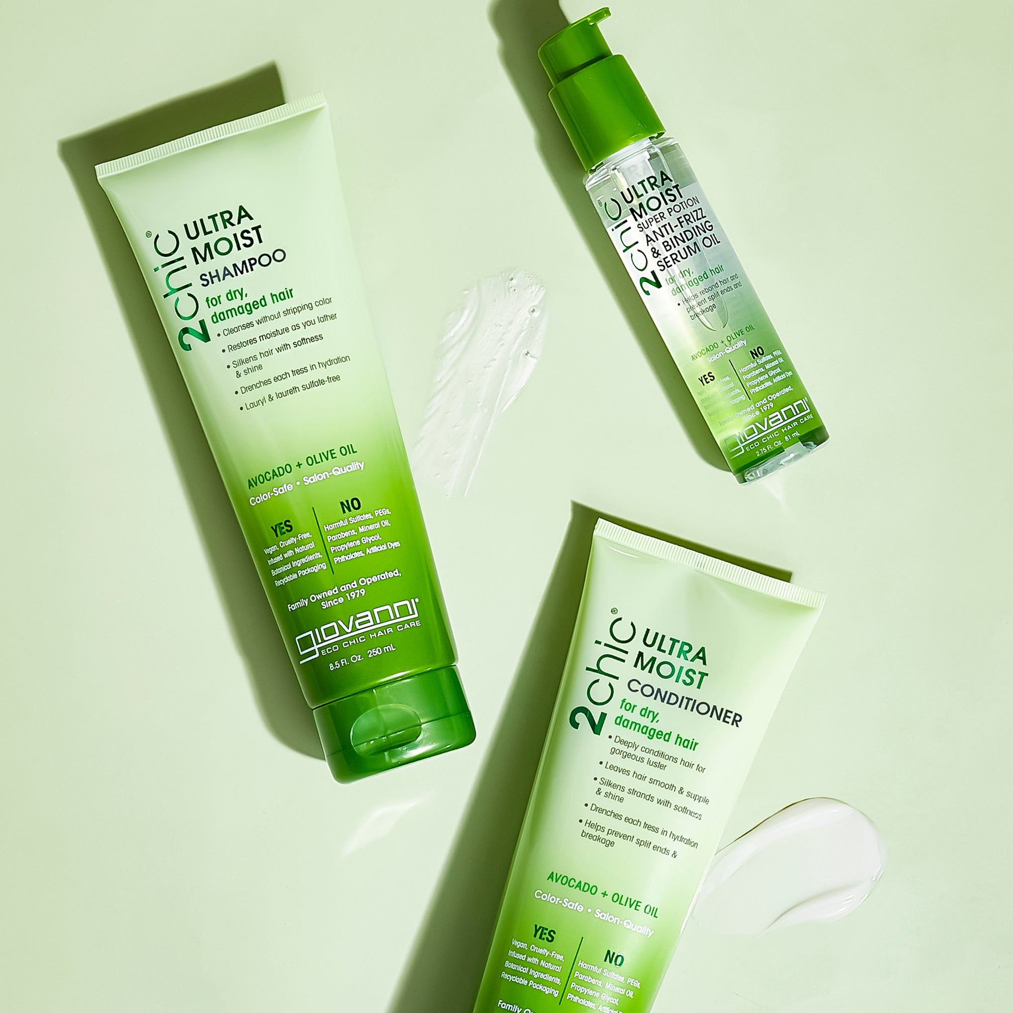 Three green bottles of Giovanni Cosmetics 2chic® ULTRA-MOIST SUPER POTION ANTI-FRIZZ & BINDING SERUM OIL rest on a light green surface, each with a dollop of product nearby.