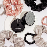 The Giovanni Cosmetics SCALP MASSAGER & SHAMPOO BRUSH with a black handle rests on a white surface, surrounded by satin scrunchies in pink, black, and beige—ideal for hair care routines and relaxation.