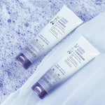 Two white and purple tubes of Giovanni Cosmetics 2chic® ULTRA-SHINE CONDITIONER lie on a blue, bubbly surface beside sheer white fabric. The packaging highlights its benefits for fine, limp hair with a dual taming complex.