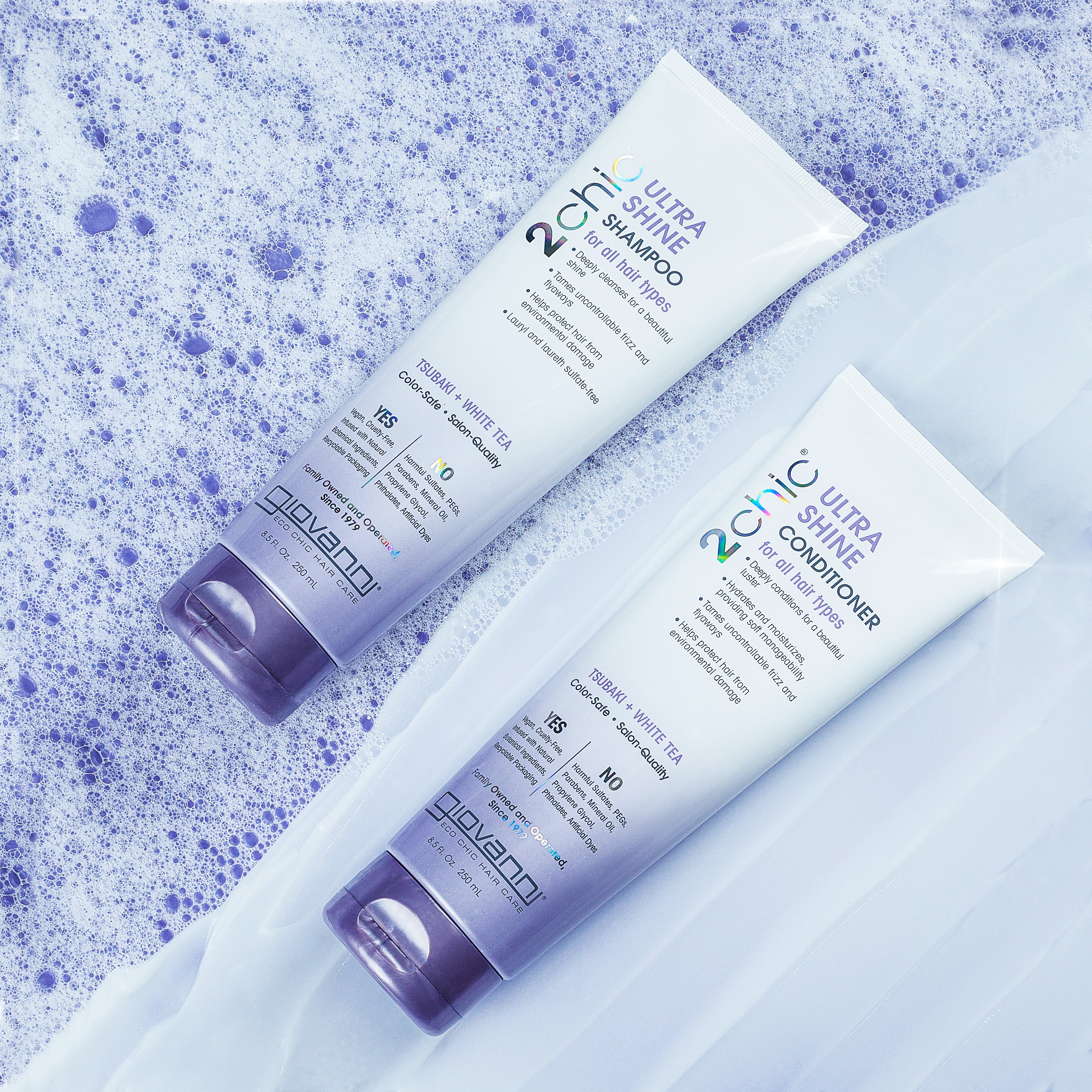 Two white and purple tubes of Giovanni Cosmetics 2chic® ULTRA-SHINE CONDITIONER lie on a blue, bubbly surface beside sheer white fabric. The packaging highlights its benefits for fine, limp hair with a dual taming complex.