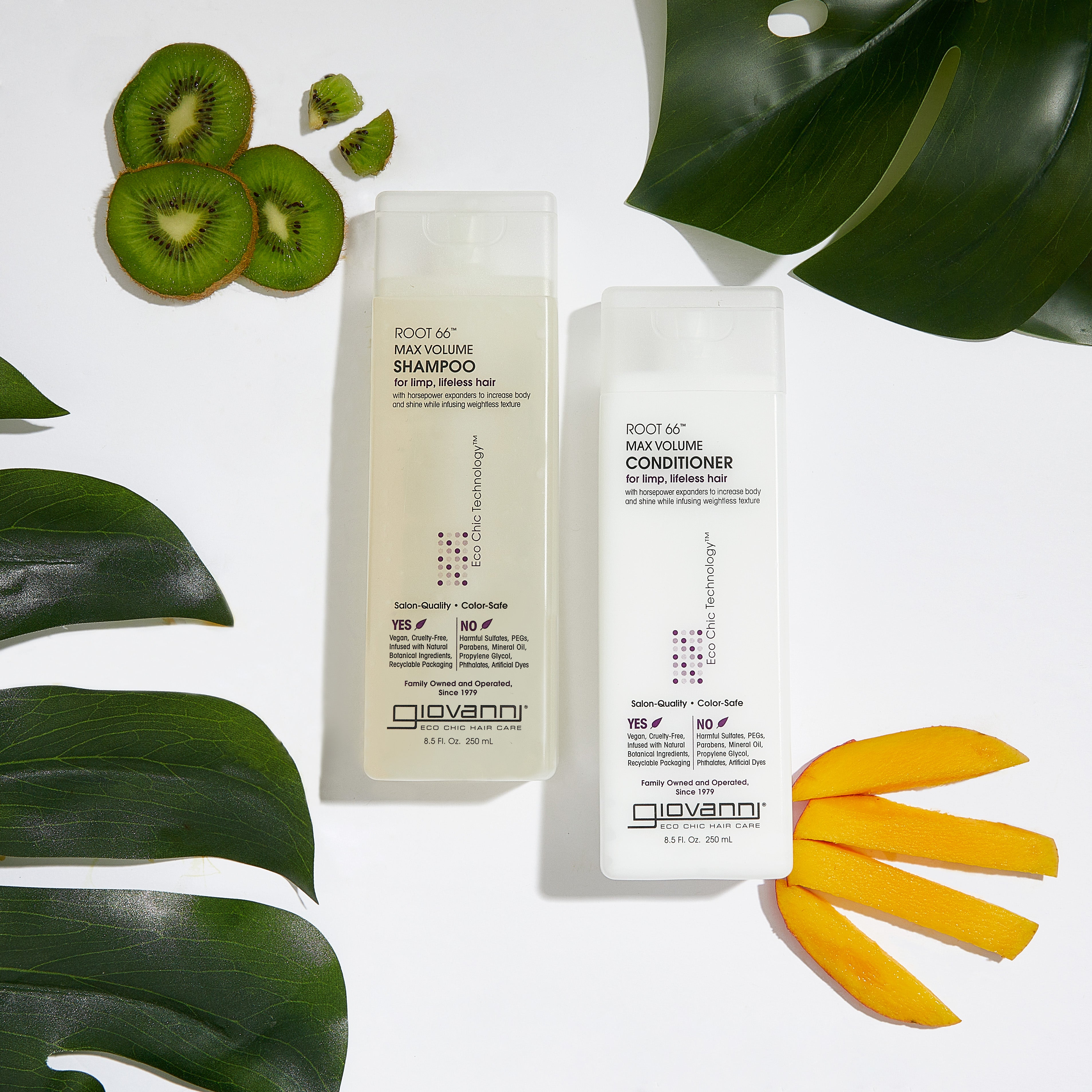 A white bottle of Giovanni Cosmetics ROOT 66™ MAX VOLUME CONDITIONER for fine, thinning hair sits on a white surface, surrounded by green leaves and fresh kiwi and mango slices.