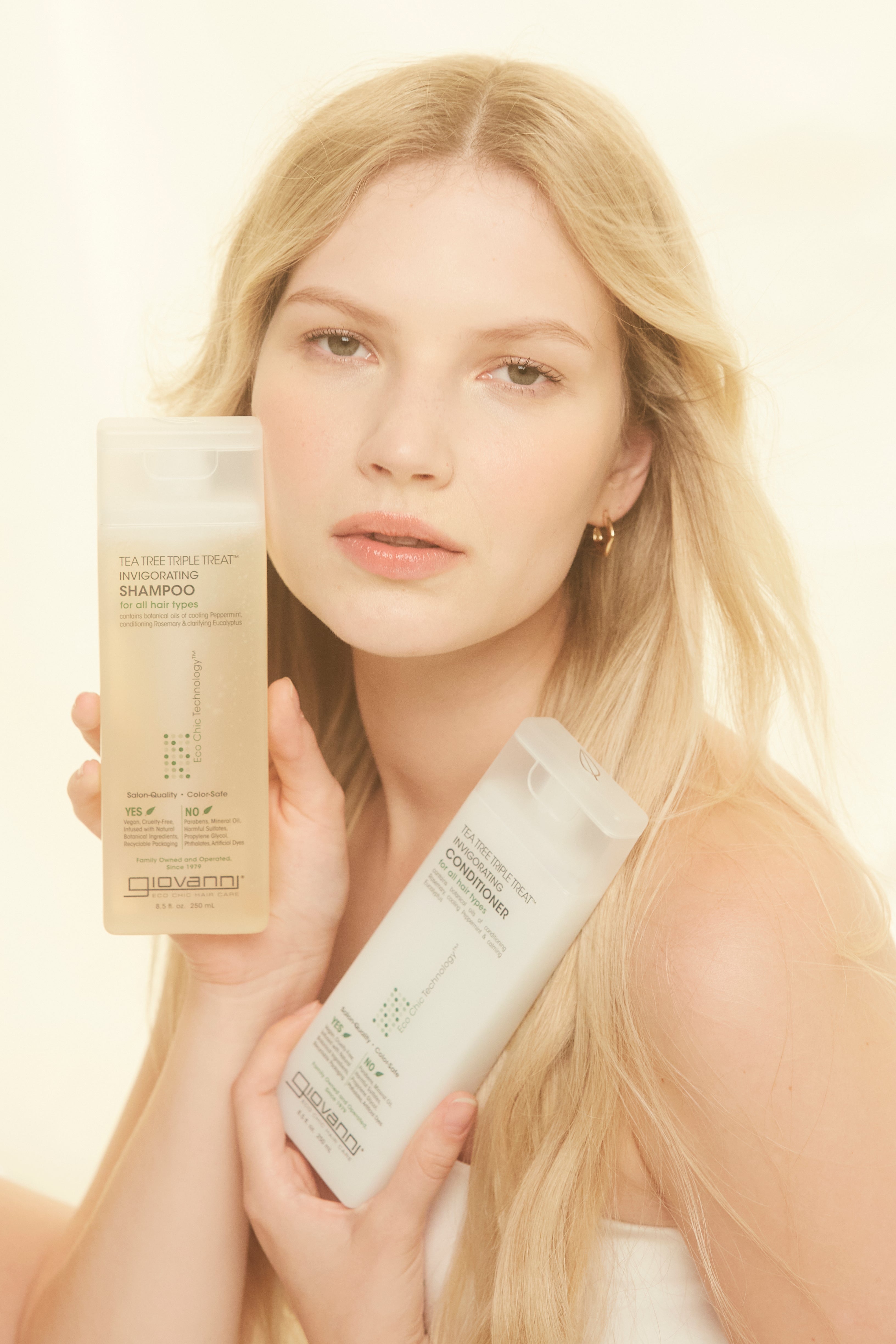 Woman holding bottles of Tea Tree Triple Treat Invigorating Shampoo and Conditioner