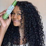Woman with curly hair holding a bottle of 2Chic Ultra Moist serum against a neutral background