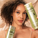 A woman with curly hair smiles softly, holding Giovanni Cosmetics Smoothing Castor Oil Conditioner in front of a beige, silky background—highlighting her frizz-taming and hair protection routine.