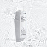 A white bottle of Giovanni Cosmetics SMOOTH AS SILK™ HAIR DETANGLING SPRAY rests on a rippled white surface with soft light reflections, creating a clean, fresh look—ideal for silky, detangled hair.