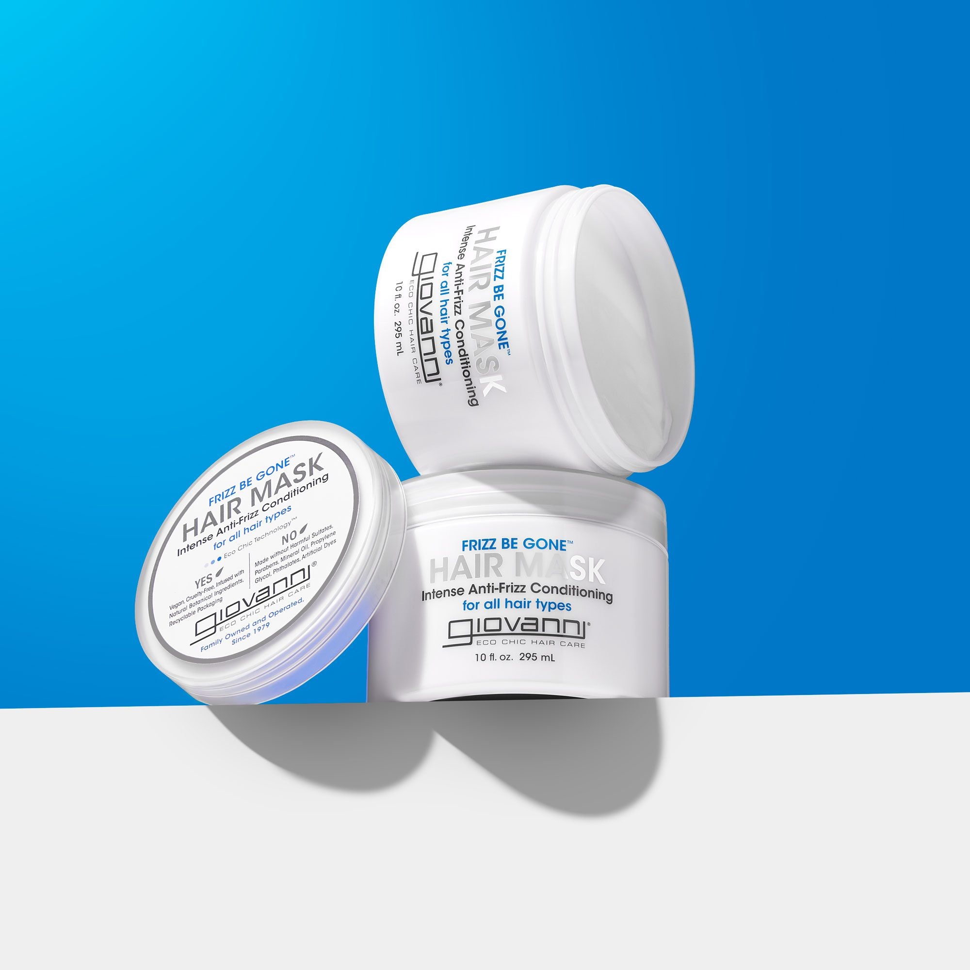 Three white jars of Giovanni Cosmetics FRIZZ BE GONE™ INTENSIVE ANTI-FRIZZ CONDITIONING HAIR MASK are stacked against a blue and white background, highlighting this deep conditioning mask for frizz control and intense hydration.