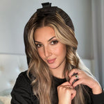 A woman with long, wavy blonde hair wears the black HEATLESS SATIN HAIR CURLING SET by Giovanni Cosmetics. Indoors and in a black top, she smiles at the camera while holding a smooth, frizz-free wave.