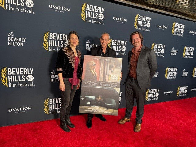 Giovanni James Guidotti on a red carpet at the Beverly Hills Film Festival holding a poster.