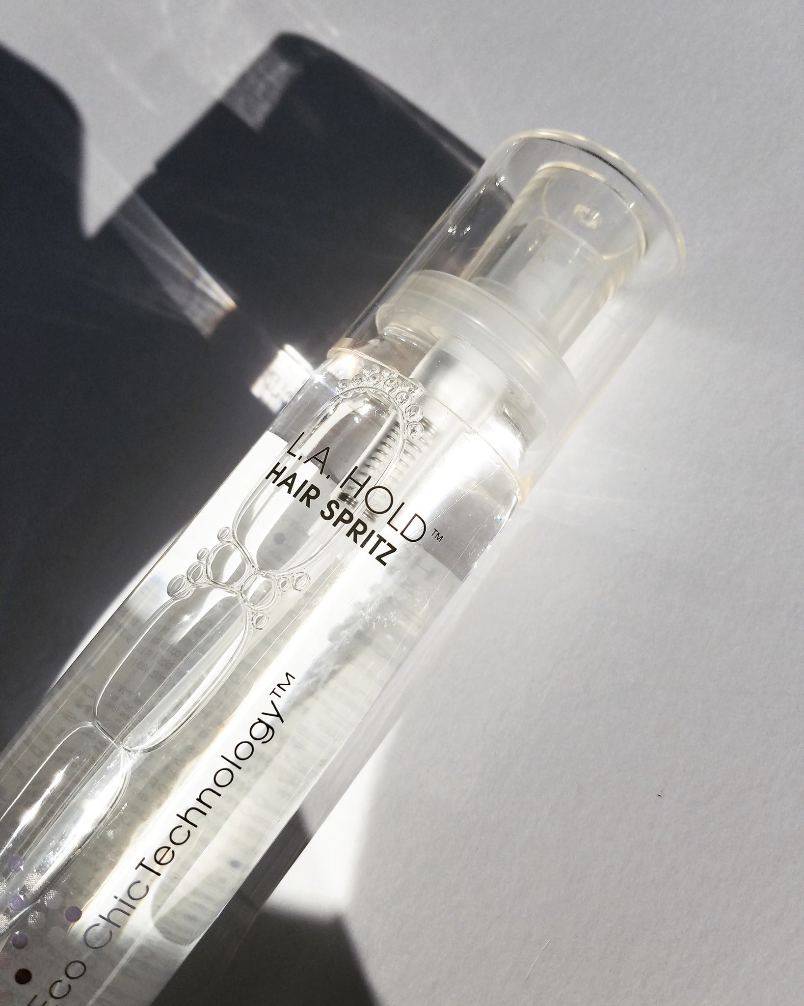 A clear bottle labeled L.A. HOLD™ HAIR SPRITZ by Giovanni Cosmetics sits on a white surface in sunlight, ideal for anyone seeking salon-quality, color-safe hair spray.