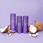 Three purple bottles of Giovanni Cosmetics CURL HABIT™ Curl Defining No-Foam Conditioning Shampoo are shown on a purple surface, surrounded by cracked coconuts and coconut pieces—ideal for moisturizing curly hair.
