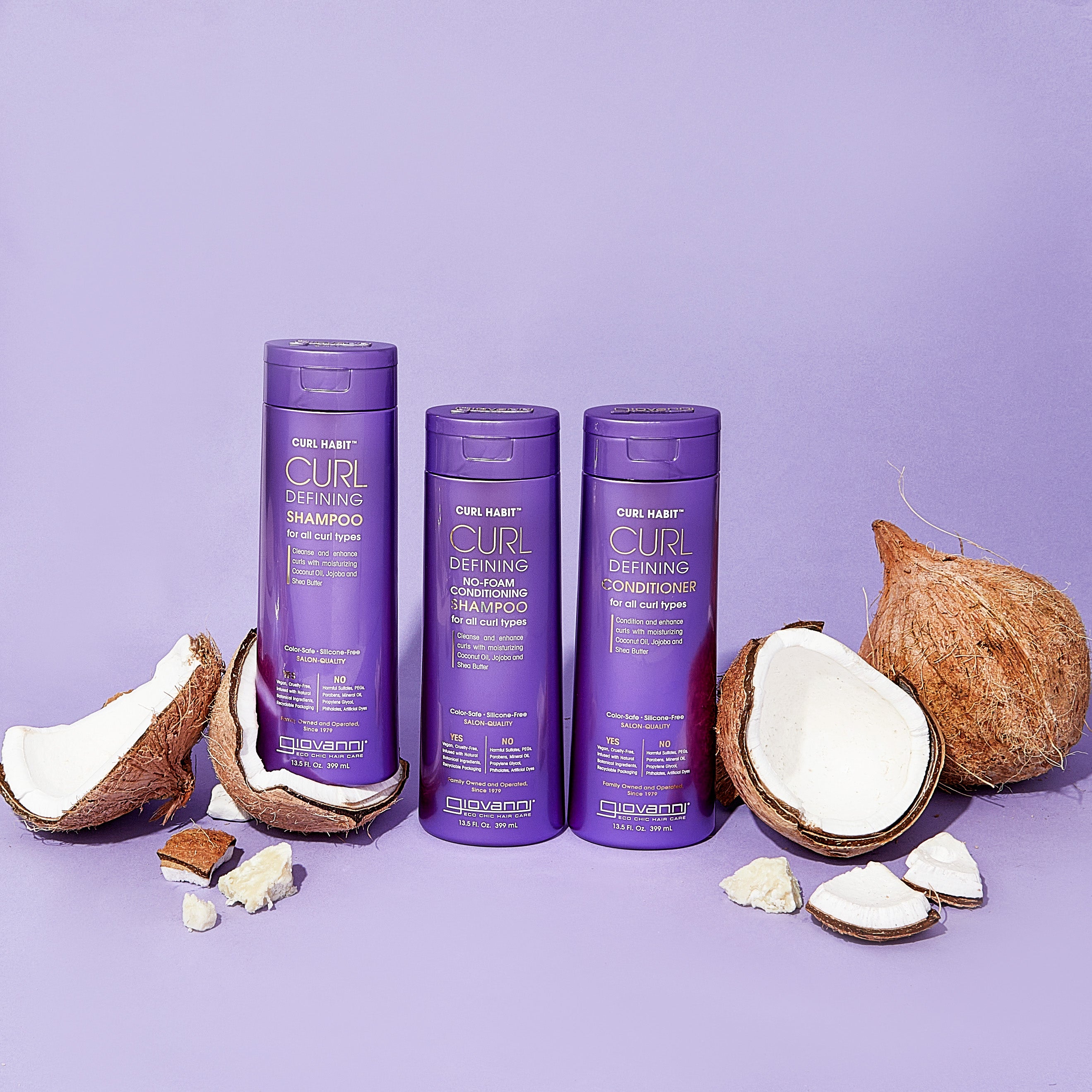 Three purple bottles of Giovanni Cosmetics CURL HABIT™ Curl Defining No-Foam Conditioning Shampoo are shown on a purple surface, surrounded by cracked coconuts and coconut pieces—ideal for moisturizing curly hair.
