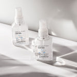 Two clear spray bottles of Giovanni Cosmetics SHINE OF THE TIMES™ HIGH GLOSS HAIR MIST rest on a white surface, illuminated by natural light with soft shadows.