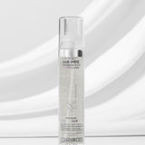 A clear bottle of Giovanni Cosmetics L.A. HOLD™ HAIR SPRITZ stands upright on a white surface against a soft gray background, displaying its visible label and color-safe, salon-quality hair spray inside.