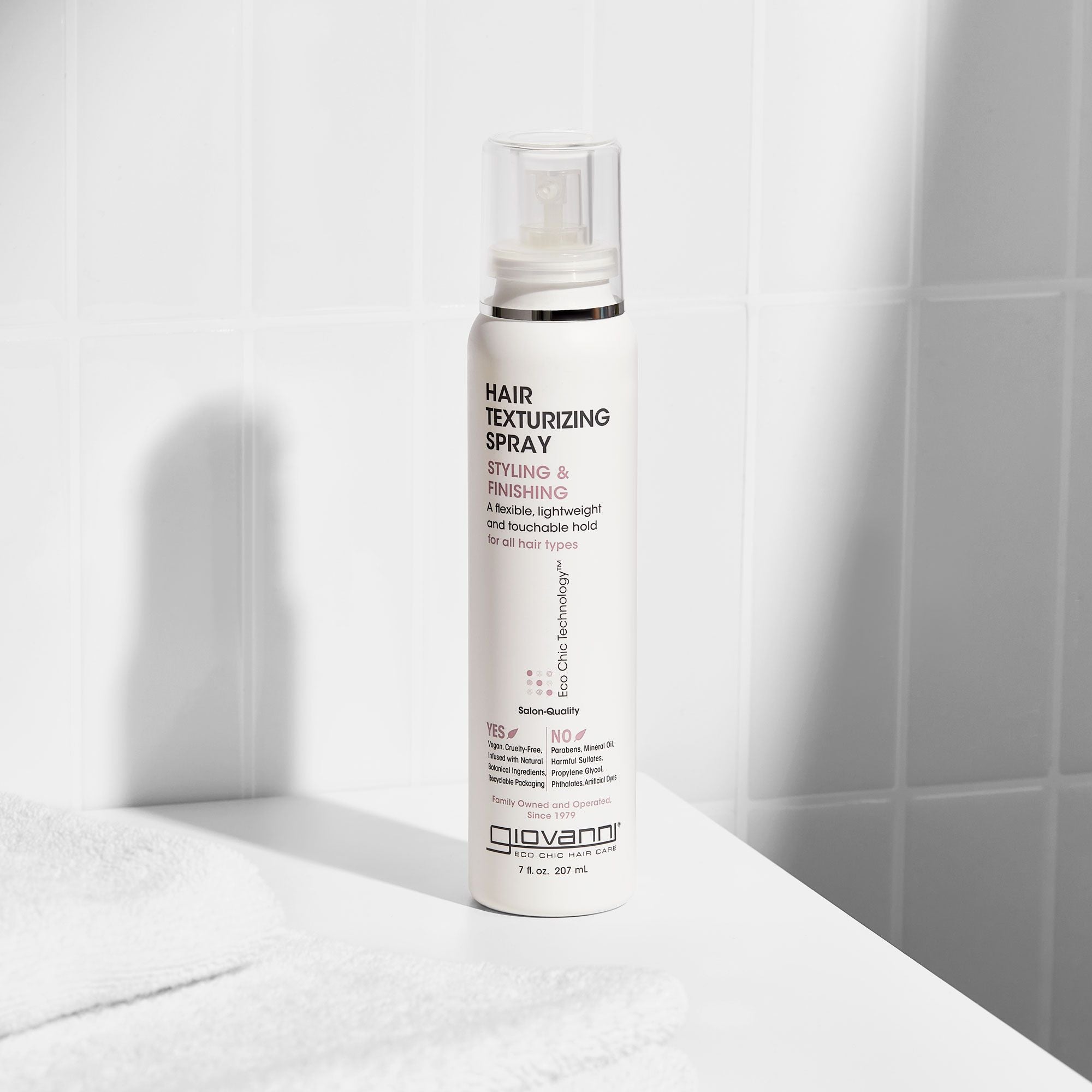 A bottle of Giovanni hair texturizing spray on a white surface with light shadows.